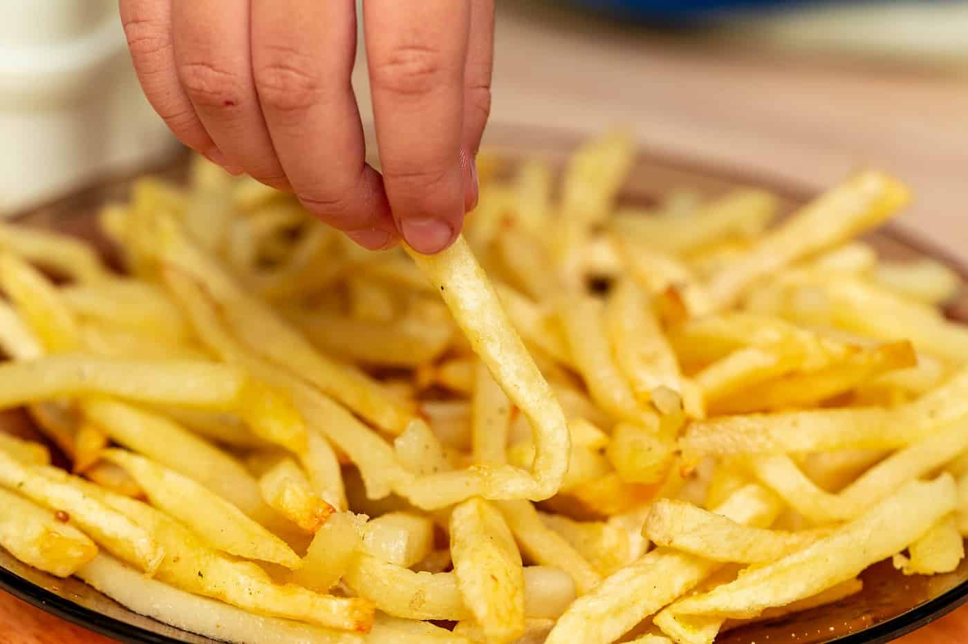 La mano de la persona busca papas fritas: comida real versus comida falsa